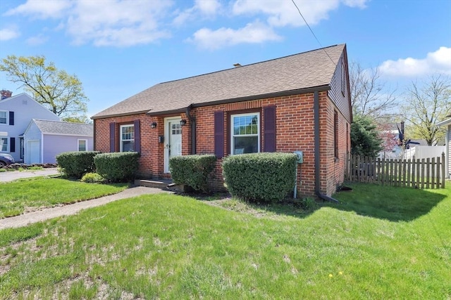 bungalow with fence, a front yard, roof with shingles, and brick siding