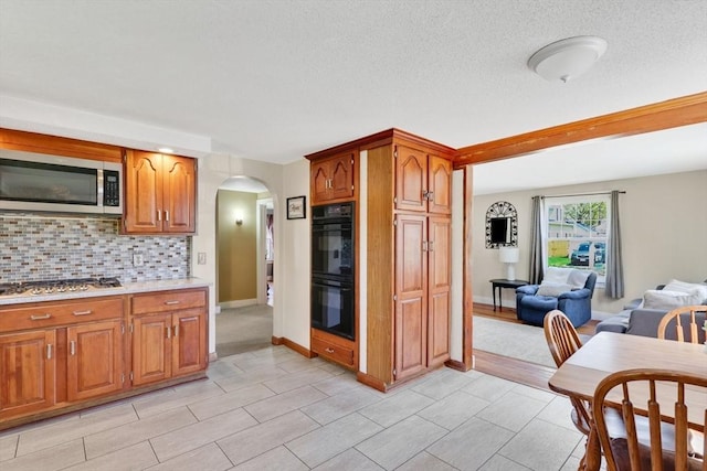 kitchen with backsplash, arched walkways, brown cabinets, light countertops, and stainless steel appliances