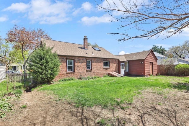 rear view of house featuring fence, a chimney, brick siding, a shingled roof, and a lawn