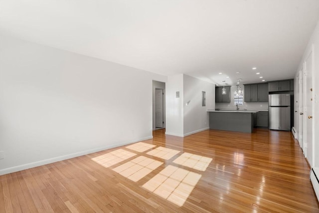 unfurnished living room featuring a baseboard heating unit, wood-type flooring, and sink