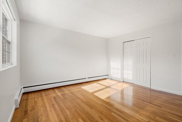 unfurnished room with a baseboard heating unit, a wealth of natural light, and light wood-type flooring