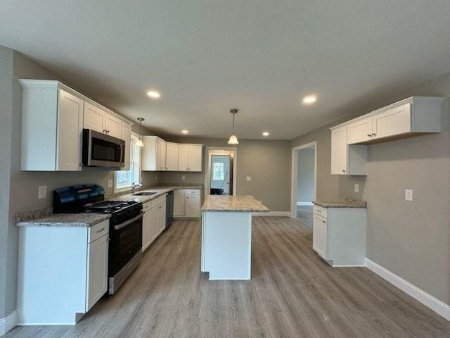 kitchen featuring stainless steel appliances, light stone countertops, white cabinets, pendant lighting, and a center island