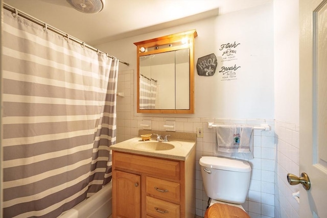 bathroom featuring shower / tub combo with curtain, toilet, tile walls, wainscoting, and vanity