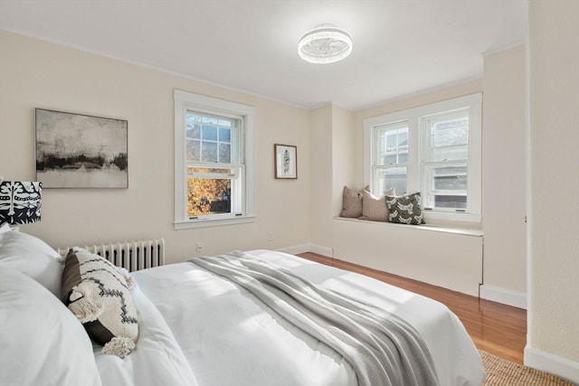 bedroom with hardwood / wood-style floors, multiple windows, and radiator