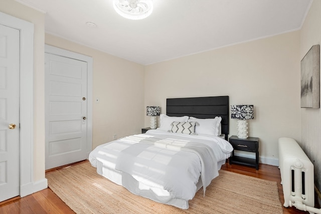 bedroom featuring light wood-type flooring, crown molding, and radiator