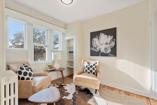 living area with built in features, wood-type flooring, crown molding, and radiator