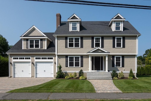 colonial home featuring a front lawn, decorative driveway, an attached garage, a shingled roof, and a chimney