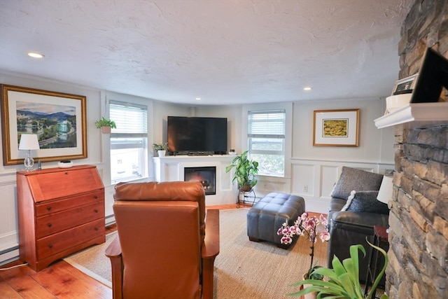 living area with plenty of natural light, a decorative wall, a glass covered fireplace, and wood finished floors