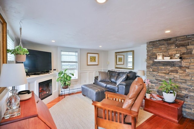 living area featuring a baseboard heating unit, a glass covered fireplace, wainscoting, and wood finished floors
