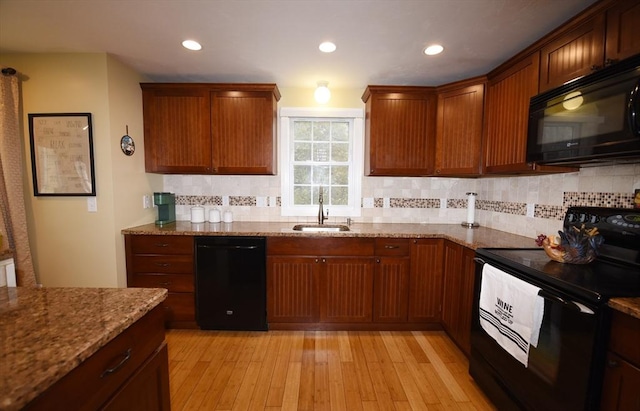 kitchen with tasteful backsplash, light wood-style flooring, light stone countertops, black appliances, and a sink