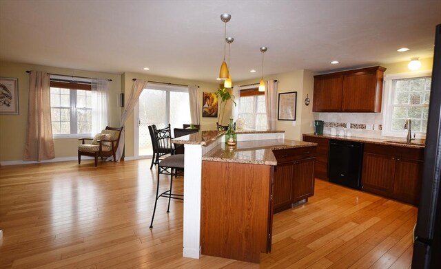 kitchen with black dishwasher, a breakfast bar, light stone countertops, light wood-style floors, and a sink