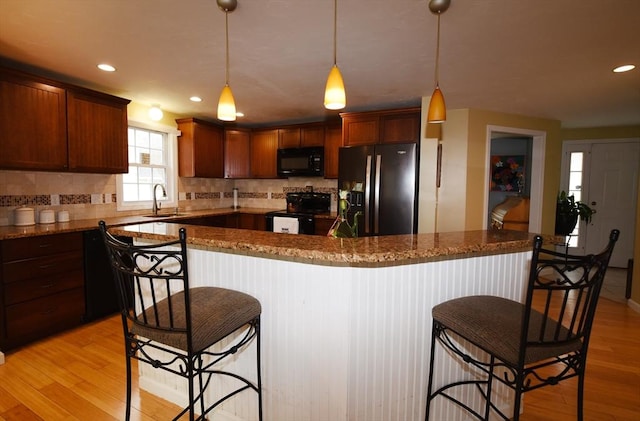 kitchen featuring a sink, decorative backsplash, black appliances, light wood finished floors, and a kitchen bar