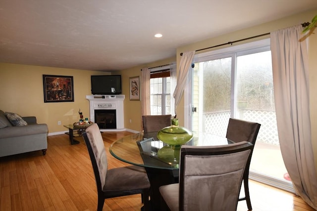 dining area featuring light wood-style floors, baseboards, a fireplace with raised hearth, and recessed lighting