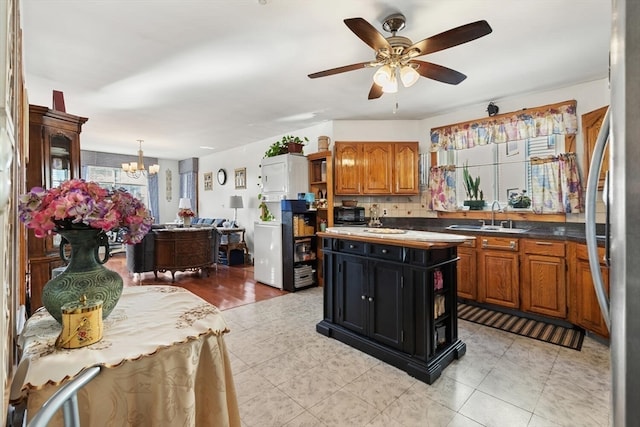 kitchen with a center island, ceiling fan with notable chandelier, sink, decorative backsplash, and stainless steel fridge