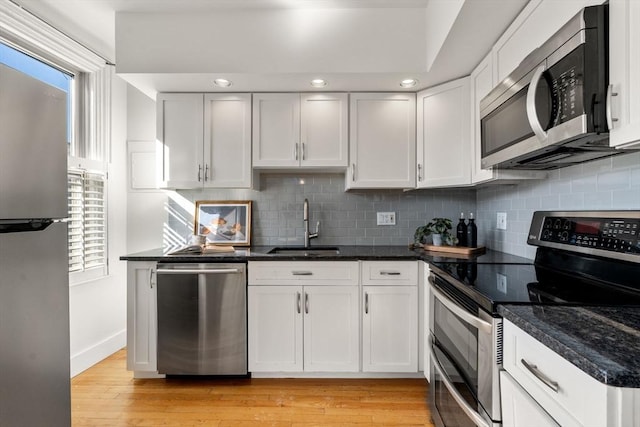 kitchen with appliances with stainless steel finishes, white cabinetry, dark stone countertops, sink, and light hardwood / wood-style flooring