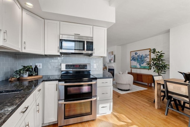 kitchen with stainless steel appliances, white cabinetry, dark stone counters, and light hardwood / wood-style floors