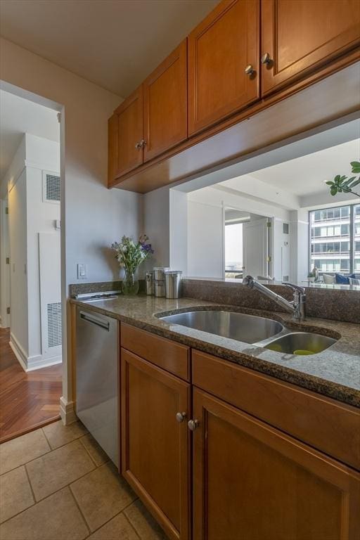 kitchen with stainless steel dishwasher, dark stone counters, sink, and light tile patterned floors