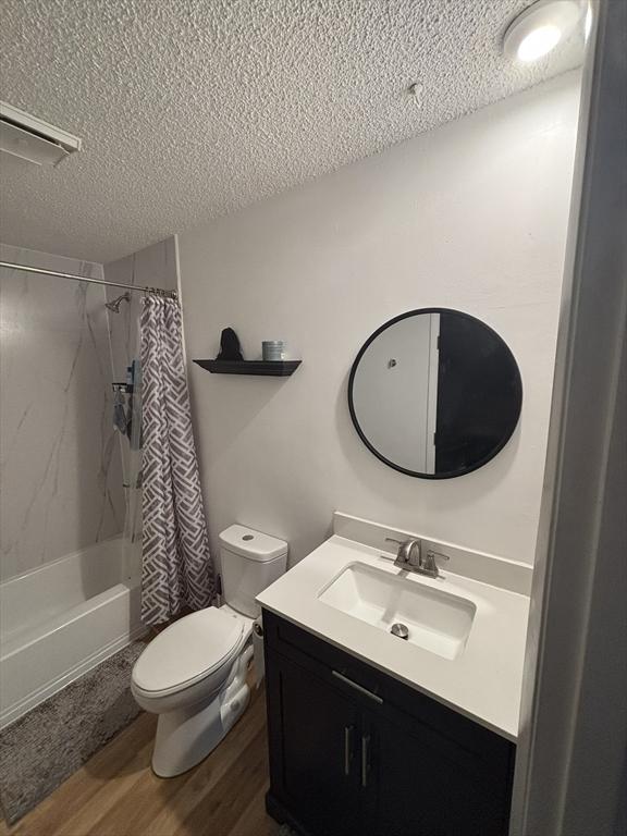 full bathroom featuring shower / bath combination with curtain, wood-type flooring, a textured ceiling, toilet, and vanity