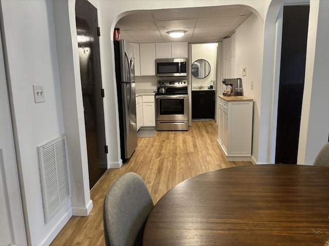 kitchen with white cabinetry, sink, a paneled ceiling, appliances with stainless steel finishes, and light wood-type flooring