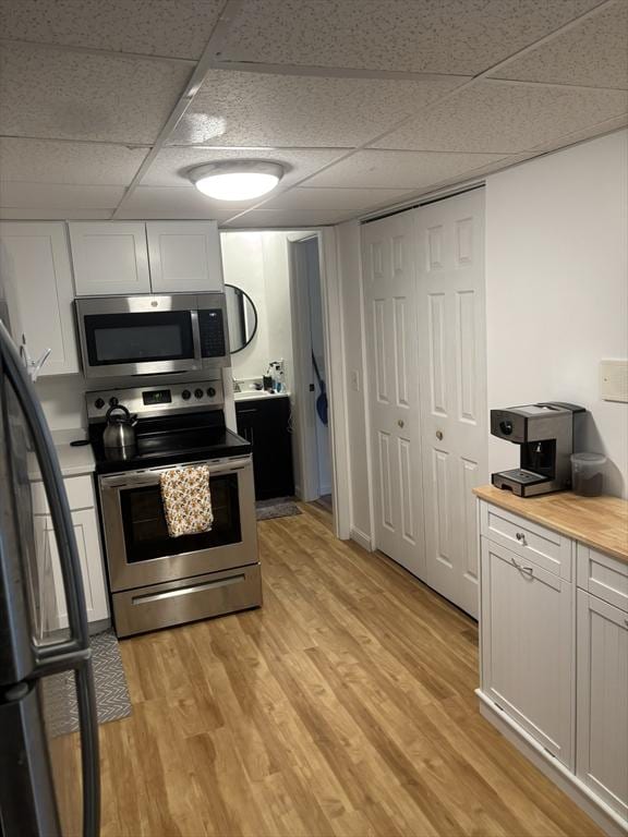 kitchen with wooden counters, a drop ceiling, stainless steel appliances, white cabinets, and light hardwood / wood-style floors