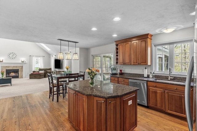kitchen featuring a sink, light wood finished floors, dishwasher, and a tile fireplace