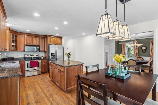 kitchen with brown cabinetry, a kitchen island, a sink, appliances with stainless steel finishes, and a notable chandelier