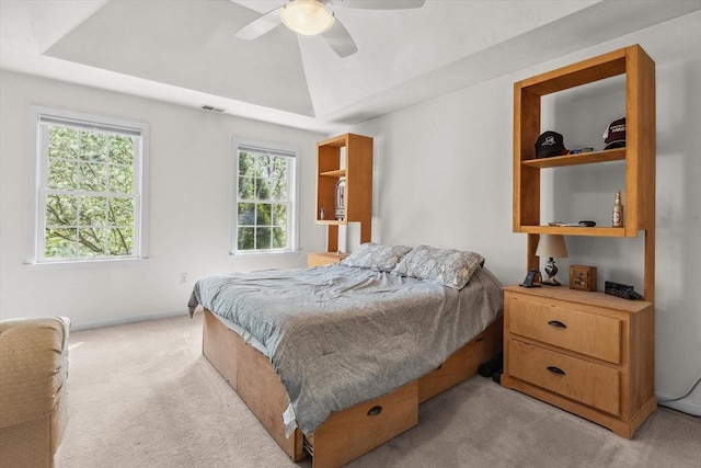bedroom with ceiling fan, light colored carpet, a raised ceiling, baseboards, and visible vents