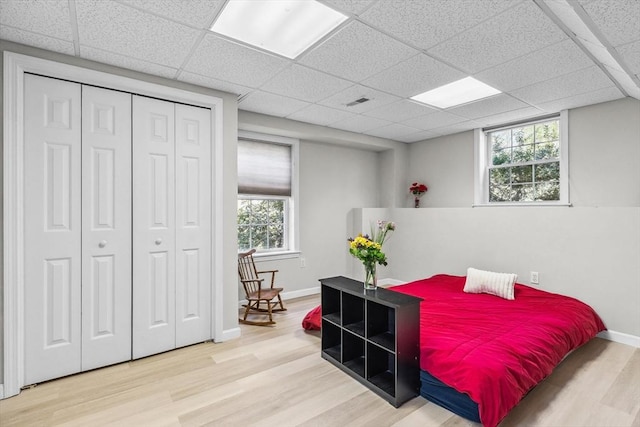 bedroom with baseboards, a paneled ceiling, wood finished floors, and multiple windows