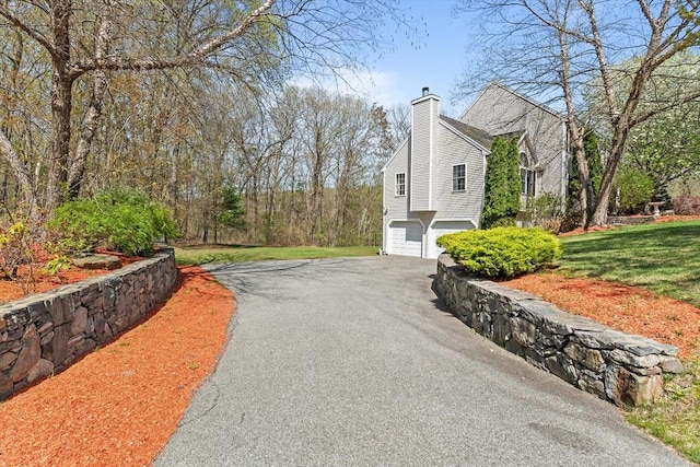 view of property exterior with a lawn, an attached garage, driveway, and a chimney