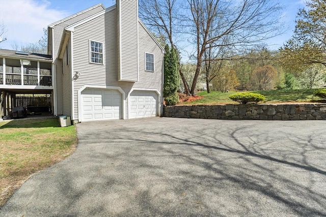 view of side of home with a garage, a chimney, a sunroom, and aphalt driveway
