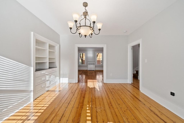 unfurnished dining area featuring a chandelier, built in shelves, light wood-type flooring, and baseboards