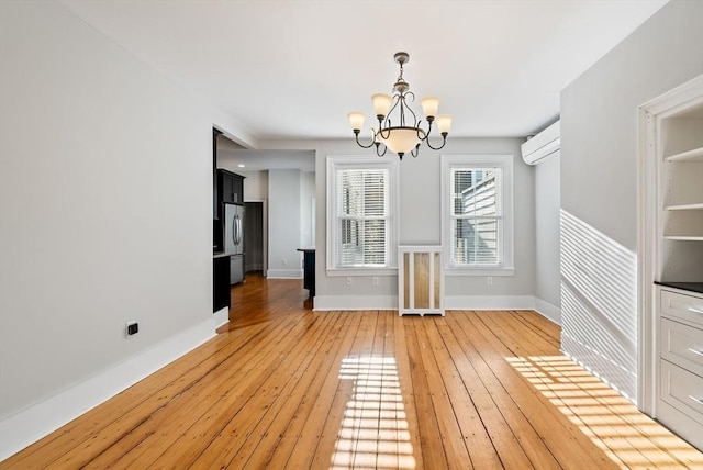 unfurnished dining area with a chandelier, a wall mounted AC, light wood-type flooring, and baseboards