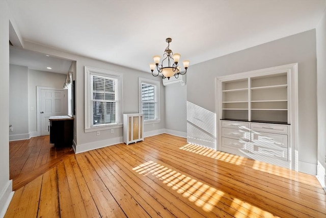 unfurnished dining area with hardwood / wood-style floors, a wall unit AC, baseboards, and a chandelier