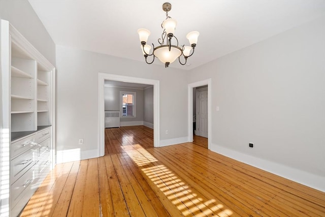 unfurnished dining area featuring a notable chandelier, light wood-style flooring, radiator, and baseboards