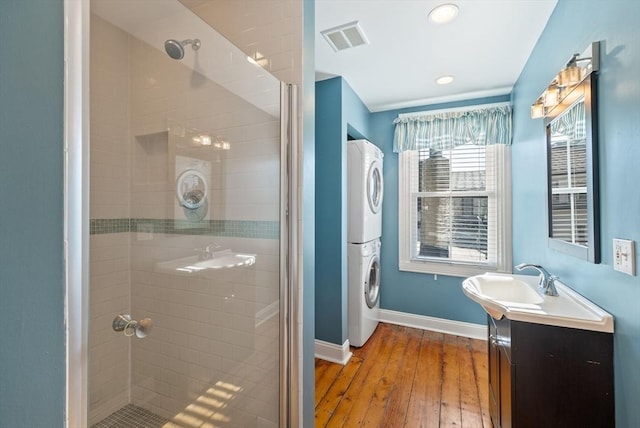 full bath with visible vents, stacked washer and clothes dryer, a stall shower, wood finished floors, and baseboards