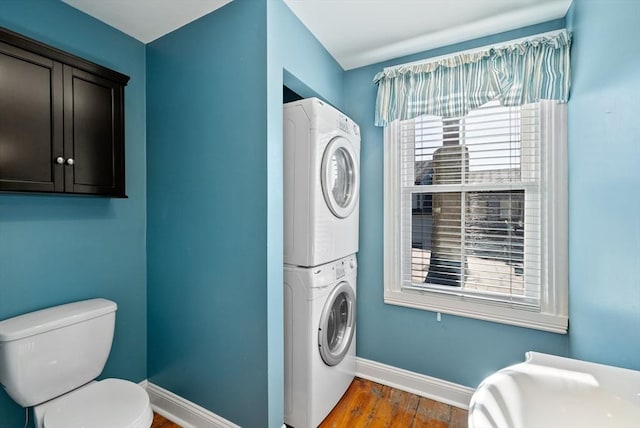 laundry area featuring baseboards, stacked washer and dryer, wood finished floors, and laundry area