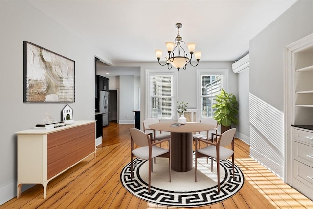 dining area featuring a wall mounted air conditioner, light wood-type flooring, baseboards, and a notable chandelier