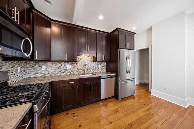 kitchen with light wood finished floors, a sink, dark brown cabinetry, appliances with stainless steel finishes, and tasteful backsplash