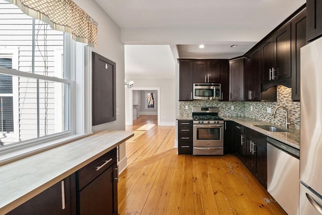 kitchen with a sink, backsplash, dark brown cabinetry, appliances with stainless steel finishes, and light wood finished floors