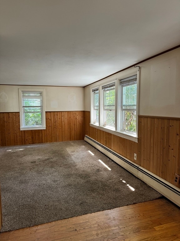 unfurnished room featuring a baseboard radiator, hardwood / wood-style flooring, and wood walls