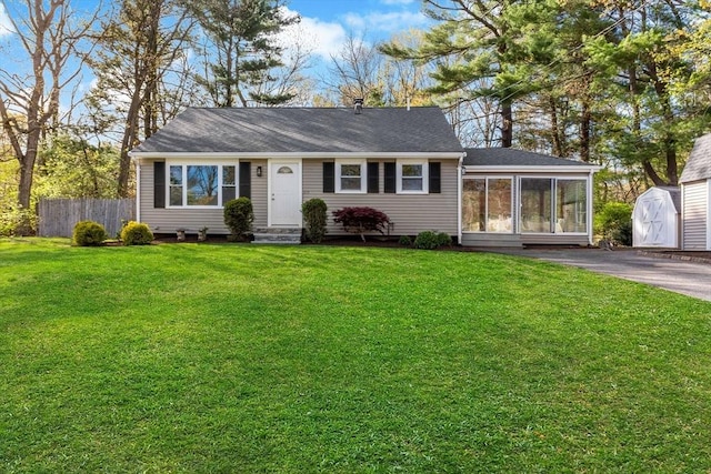 view of front of house with fence, a storage unit, an outbuilding, a front lawn, and a sunroom