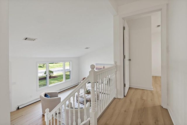 hallway with an upstairs landing, visible vents, wood finished floors, and a baseboard radiator