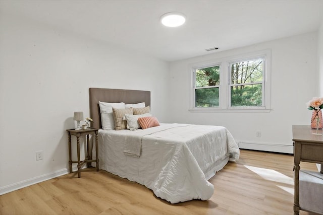 bedroom with light wood finished floors, visible vents, baseboards, and a baseboard heating unit