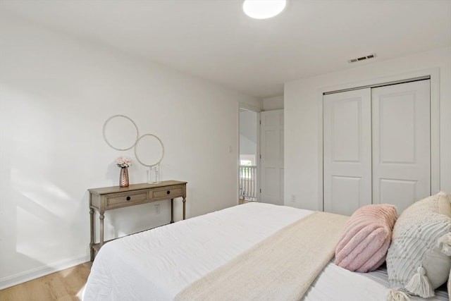 bedroom featuring baseboards, light wood-type flooring, visible vents, and a closet