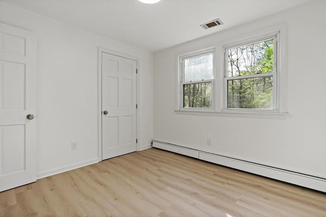 unfurnished bedroom featuring a baseboard heating unit, multiple windows, visible vents, and wood finished floors