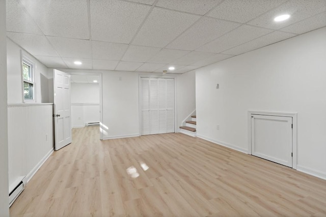 basement with stairs, light wood-type flooring, a baseboard radiator, baseboard heating, and a drop ceiling