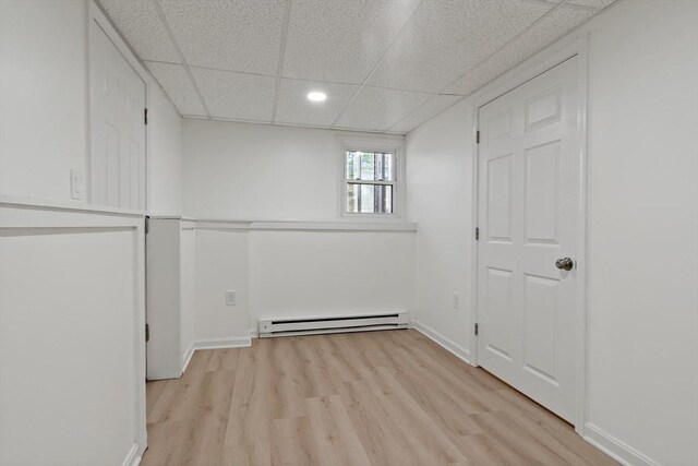 below grade area featuring a baseboard radiator, recessed lighting, baseboards, light wood finished floors, and a paneled ceiling