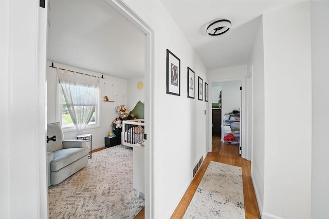 hallway featuring visible vents, baseboards, and wood finished floors