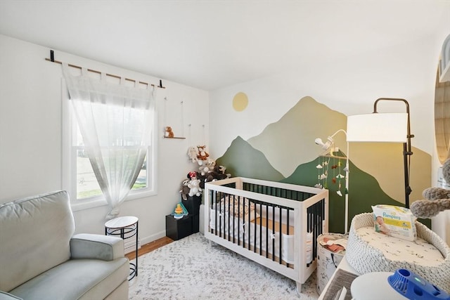 bedroom with a crib, baseboards, and wood finished floors