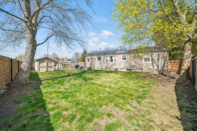 rear view of house with roof mounted solar panels, a fenced backyard, a yard, an outbuilding, and a storage unit